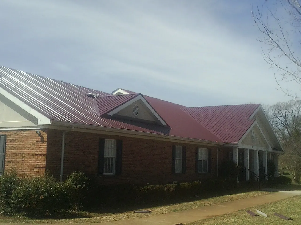 Red metal roof with gabled entries on a long brick building, from a Hail Damage Roof Repair job in Munfordville