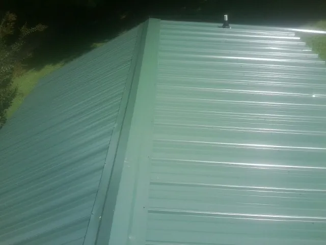 New green metal panels meeting at the ridge of a roof — Flat Roof Repair work by our crew in Munfordville