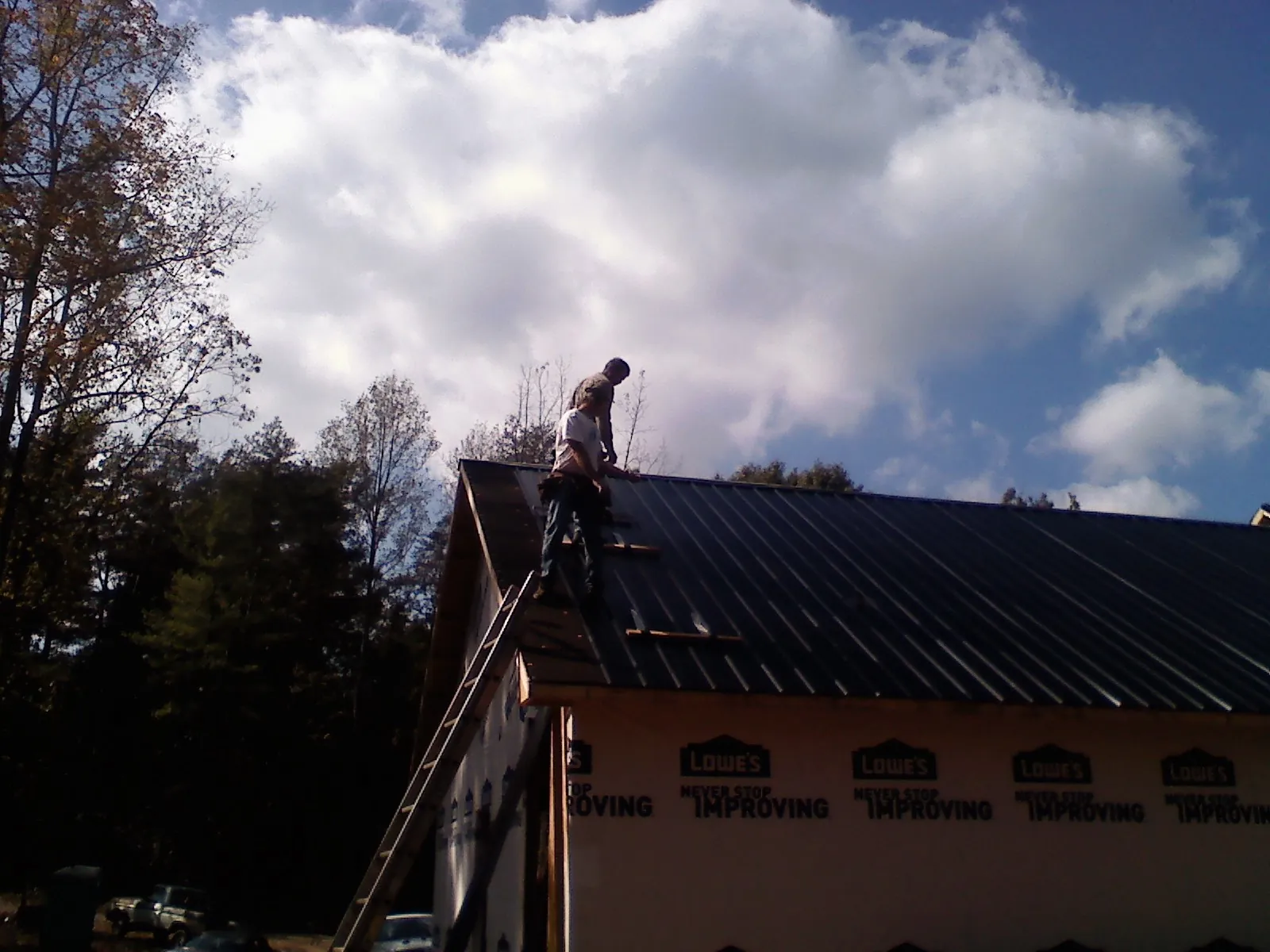 Roofer fastening dark metal panels high against a cloudy sky, from a Roof Inspection job in Munfordville