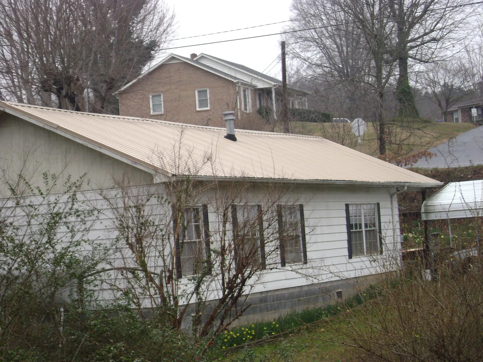 Tan metal roof on a white sided house set into a hillside — Commercial Roofing by Roofing Brothers in Munfordville